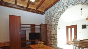 Ein Wohnzimmer mit Steinwand, Holzmöbeln, einem Fernseher und einer Essecke mit Tisch und Stühlen.