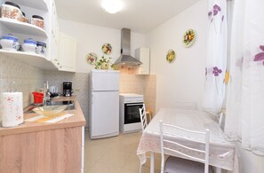 A compact kitchen with a refrigerator, stove, and sink. There is a dining table with chairs and a white tablecloth.