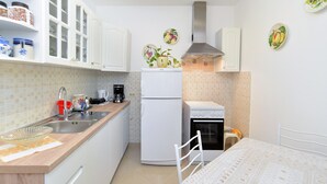 Eine kleine Küche mit weißen Schränken, einer Spüle, einem Kühlschrank und einem Herd. An der Wand befinden sich dekorative Teller und ein kleiner Tisch mit einem Stuhl.