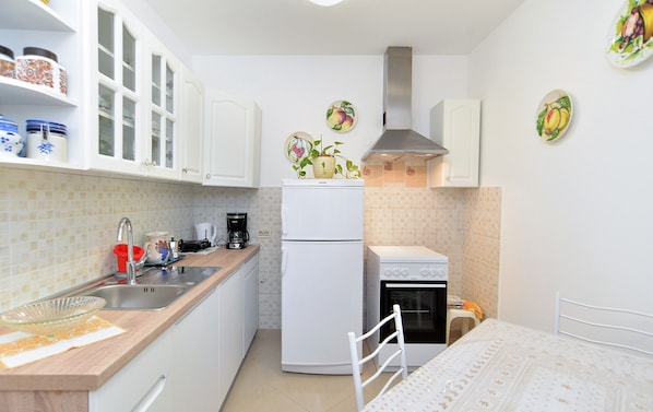 Efficient kitchen with white cabinetry, stove, sink, and refrigerator, perfect for meal preparation.