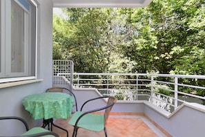 Enjoy the serene view of lush greenery from this balcony with a comfortable seating area.