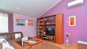 A living room with a sofa, coffee table, TV, bookshelf, and artwork on the walls. - Apartment 1917 (Rovinj)