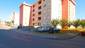 Un immeuble d’appartements à plusieurs étages, doté d’un toit plat, de balcons et d’un espace de stationnement où sont garées des voitures.