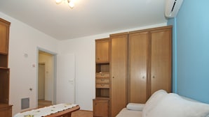 Quarto com guarda-roupa de madeira, sofá branco, mesa de madeira com toalha e luminária no teto.