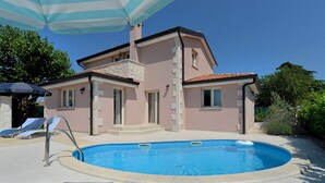Ein zweigeschossiges Haus mit Swimmingpool, Steinstufen und einer gefliesten Terrasse mit Liegestühlen.
