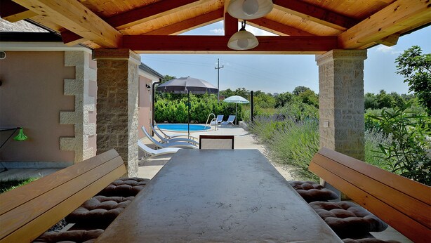 Ein überdachter Außenbereich mit Pool im Hintergrund.