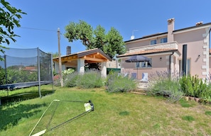 A residential property with a covered patio, a stone oven, and a well-maintained garden with various plants and a trampoline. - House 1924 (Porec)