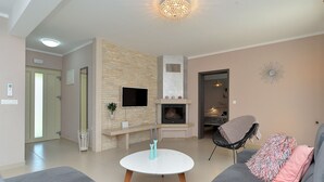 Ein Wohnzimmer mit Kamin aus Stein, einem Flachbildfernseher, einem runden Couchtisch und einem grauen Sofa mit einem rosafarbenen Kissen.