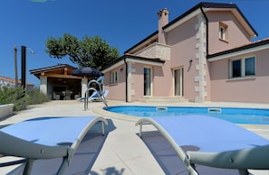 A poolside area with lounge chairs, a pool, and a building with stone facade and windows. - House 1924 (Porec)