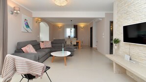 Ein modernes Wohnzimmer mit grauem Sofa, einem runden Couchtisch und einem Flachbildfernseher, der an einer Steinwand angebracht ist.