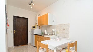Una cuina petita amb nevera, microones, cafetera i taula de menjador amb cadires.