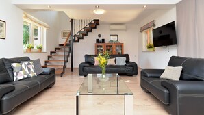 A modern living room with two black leather sofas, a glass coffee table, a staircase, and a flat-screen TV mounted on the wall. - House 1926 (Liznjan)