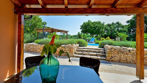 A patio area with a table, chairs, a stone wall, and a view of a pool and garden. - House 1926 (Liznjan)