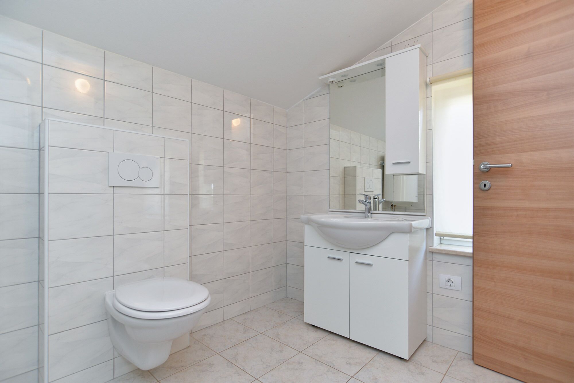 A bathroom with a toilet, a sink with a mirror, and a wooden door.