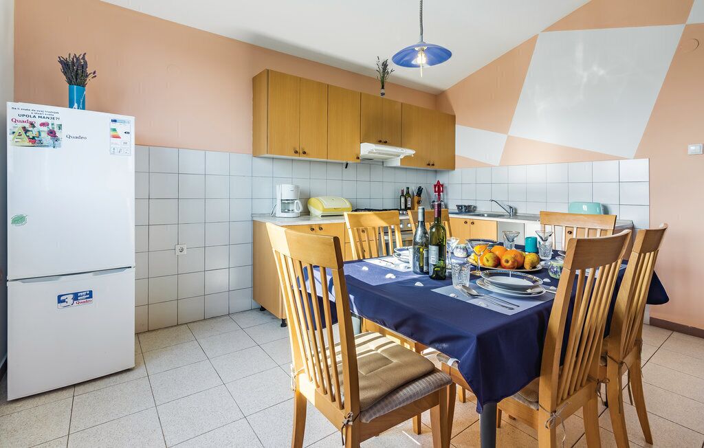A compact kitchen with a dining table set for four, wooden cabinets, a refrigerator, and a blue ceiling light.