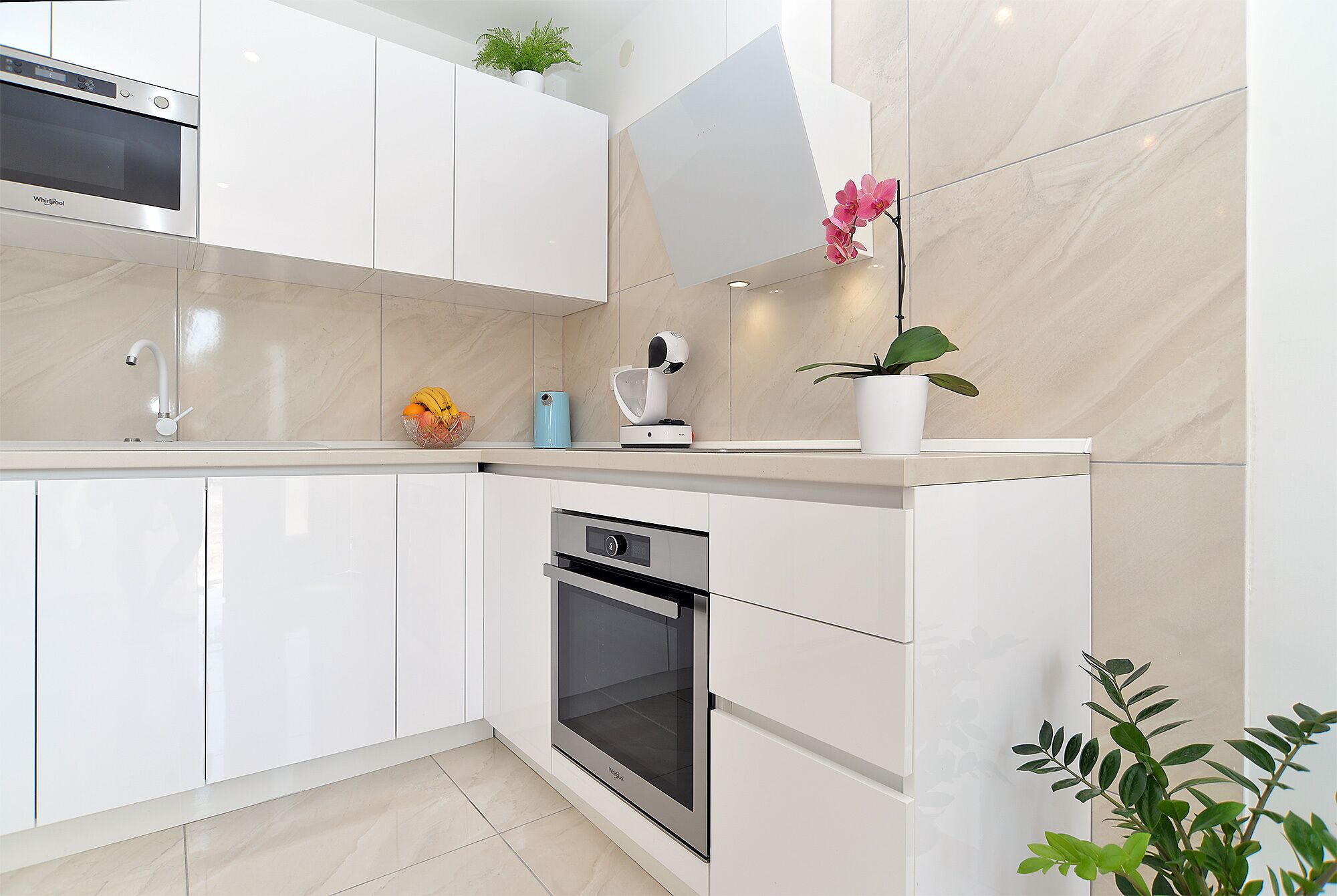 A modern kitchen with white cabinetry, a built-in oven, a microwave, and a coffee machine.