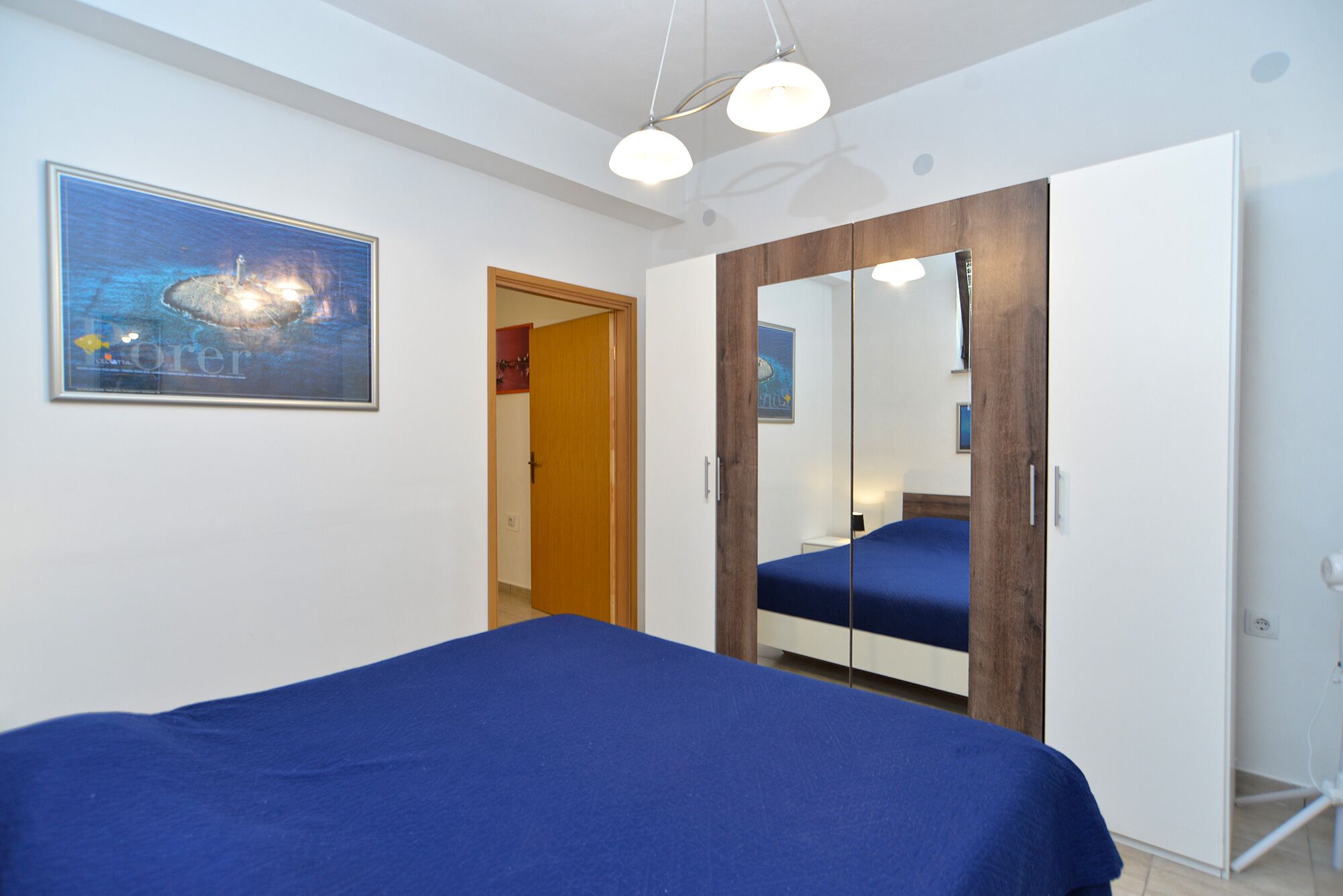A bedroom with a bed, a wardrobe, a door, and a painting on the wall.