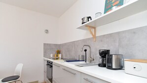 Ett kompakt kök med en vit bänkskiva, en kaffebryggare, en vattenkokare och en brödrost.