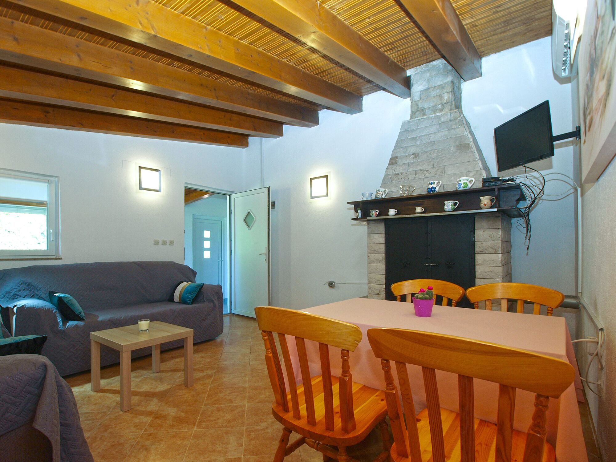 Un accogliente soggiorno con camino, travi in legno a soffitto, un tavolo da pranzo con sedie e un divano con cuscini.