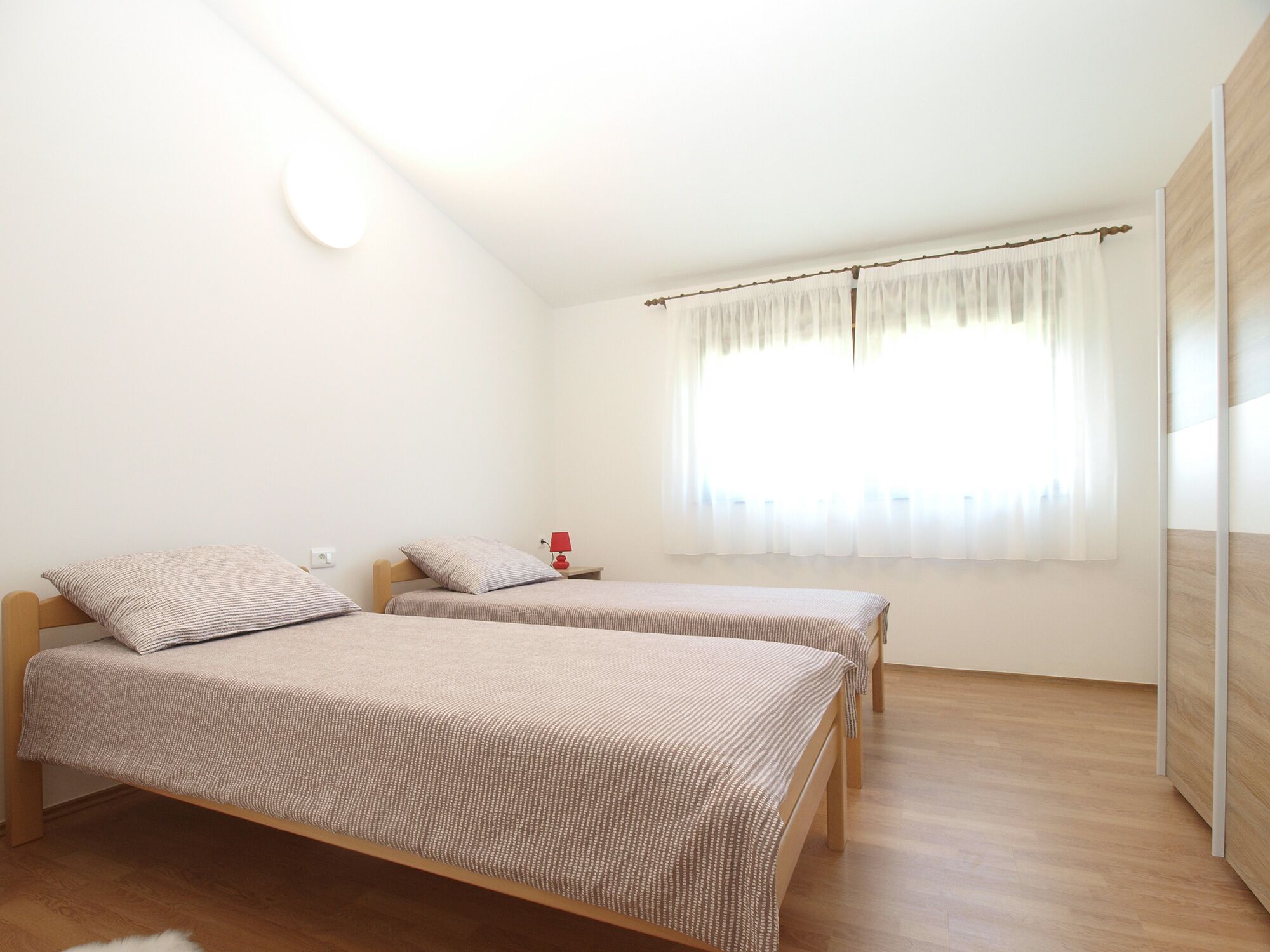 Un dormitorio con dos camas, una mesita de noche con lámpara y un ventanal con cortinas.