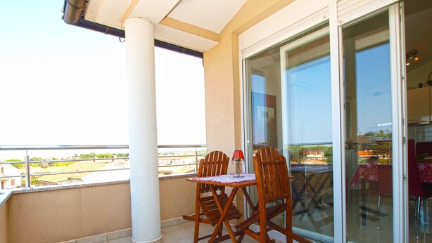 A balcony with a table and chairs, a glass door leading to an indoor area, and a view of the surrounding area. - Apartment 1932 (Fazana)