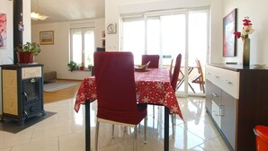 A dining area with a table set for two, a red chair, and a stove in the corner. - Apartment 1932 (Fazana)