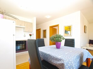 A dining area with a table covered in a blue polka dot tablecloth, surrounded by four black chairs. A purple vase with a plant is on the table.