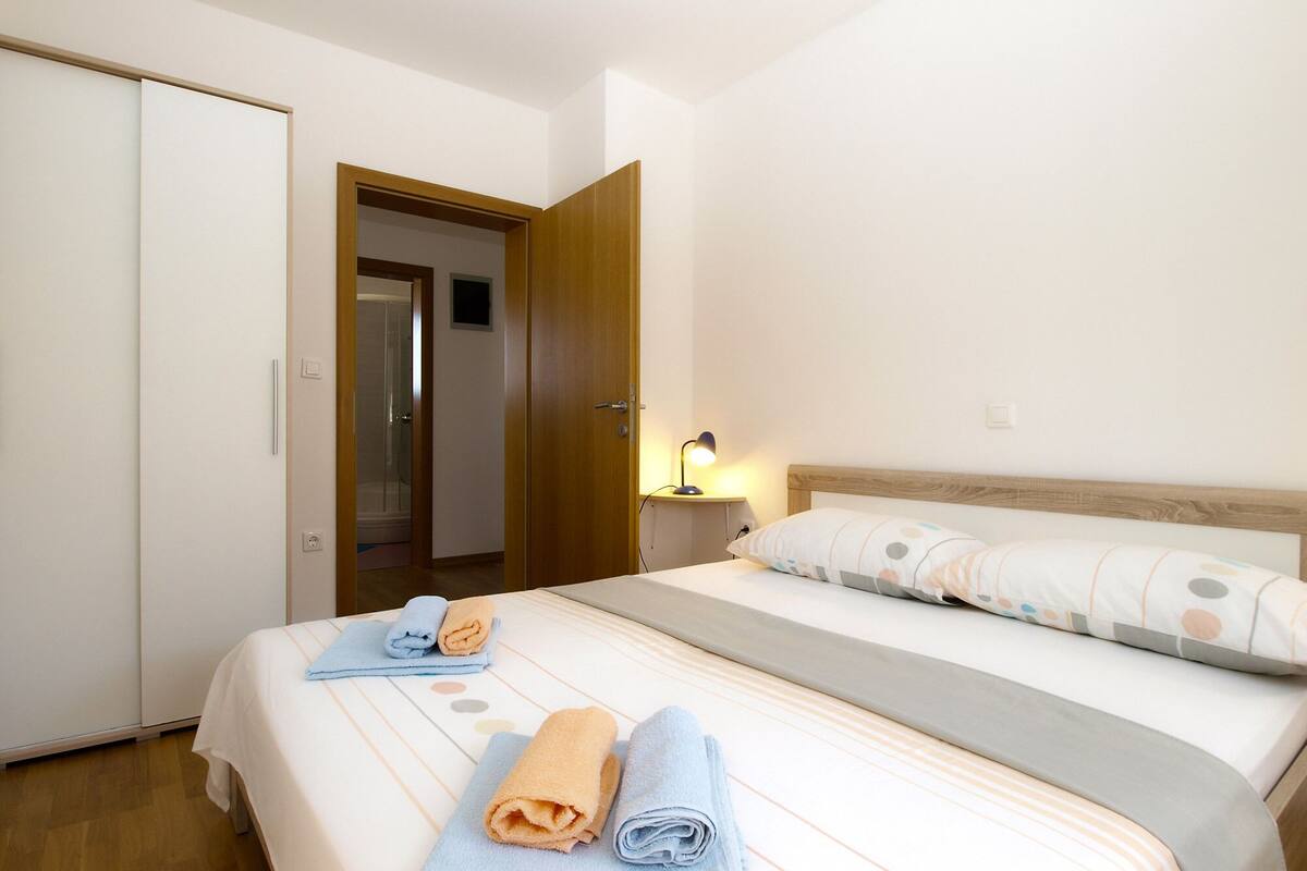 A hotel room with a bed, a nightstand with a lamp, a wardrobe, and a door leading to a bathroom.