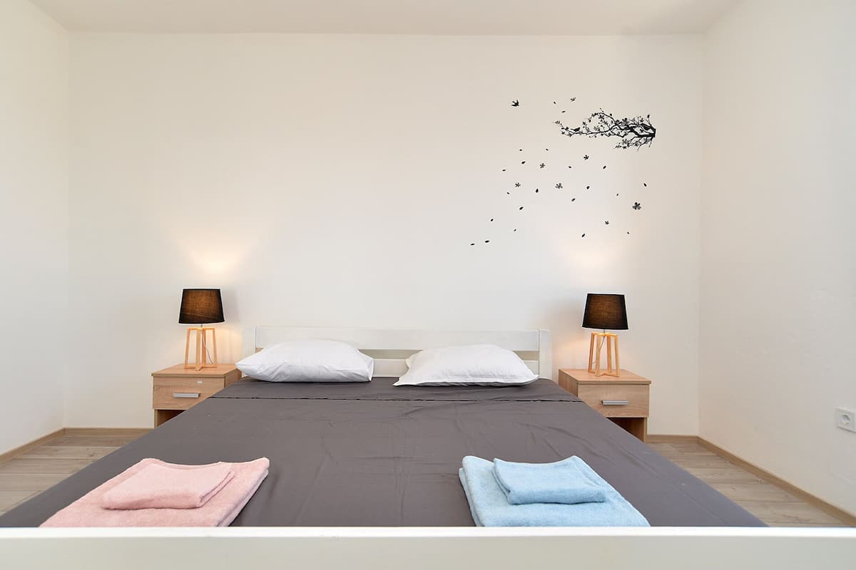 Une chambre à coucher avec un lit, deux tables de chevet avec des lampes et une décoration murale représentant des oiseaux.