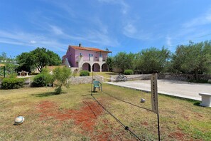 A pink villa with a red-tiled roof, stone arches, and a tennis court.