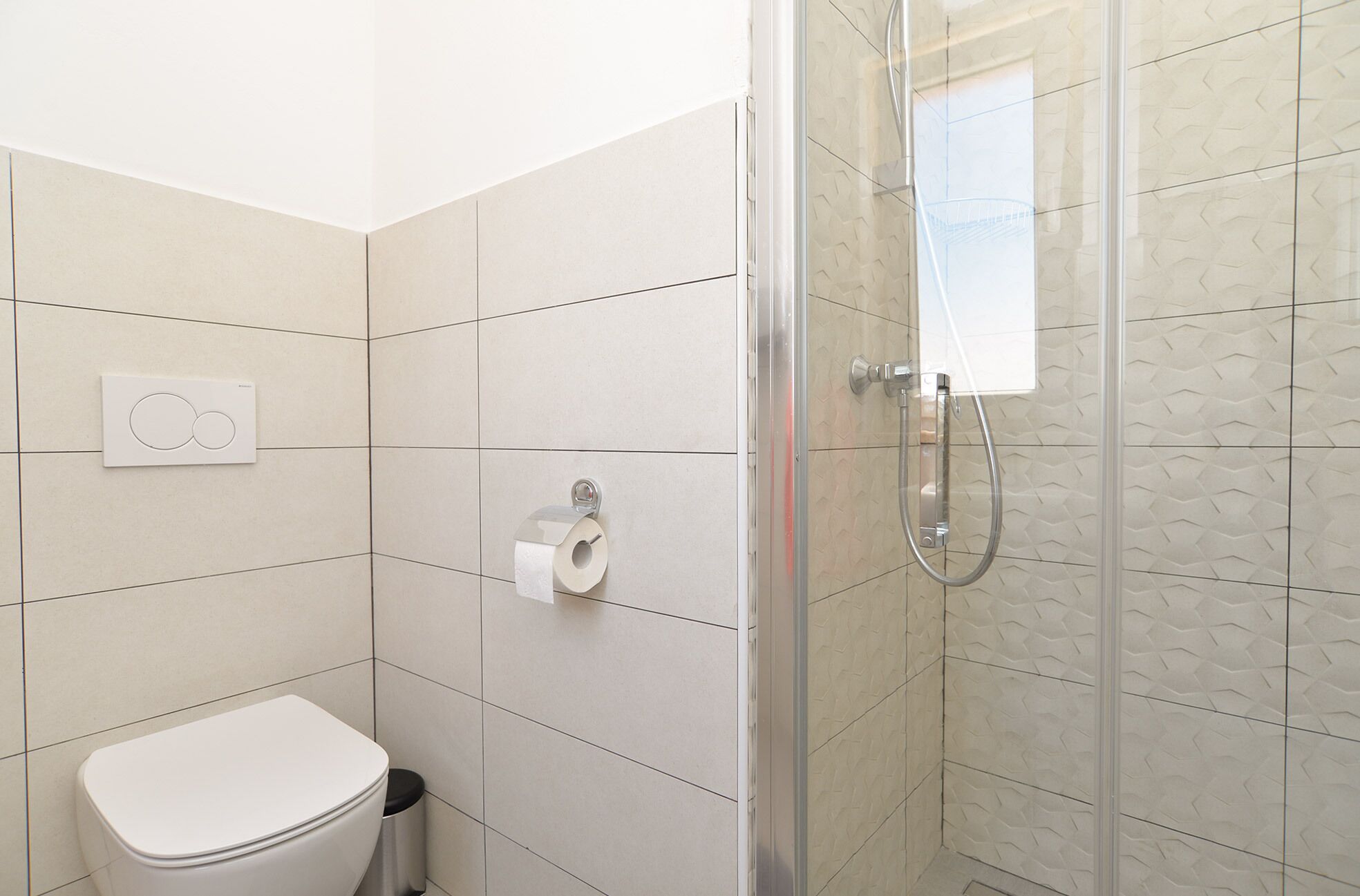 A bathroom with a toilet, a shower, and a toilet paper holder.