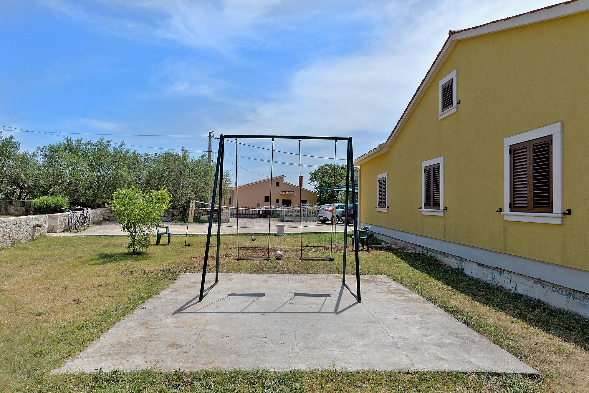 A concrete patio with a swing set, a yellow building with shutters, and a stone wall.