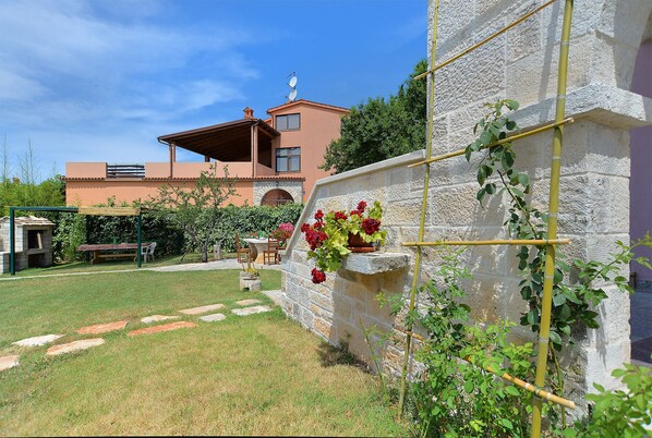A stone wall with a climbing plant, a garden with stepping stones, and a building with a sloped roof and satellite dish.