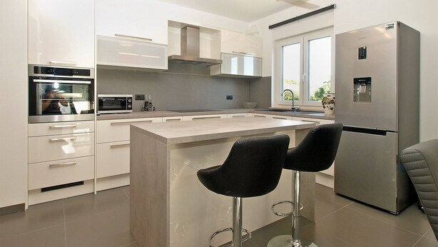 A modern kitchen with stainless steel appliances, a central island, and two bar stools. - House 1939 (Pula)