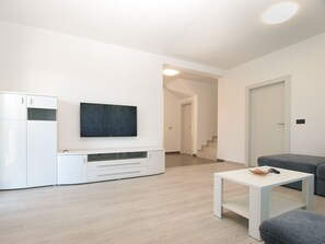 En moderne stue med et fladskærms-tv monteret på v æggen, et hvidt skab, en grå sofa og et lille hvidt bord.