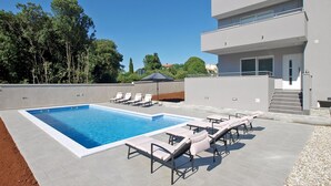 A modern outdoor pool area with lounge chairs and a building with a balcony. - House 1939 (Pula)