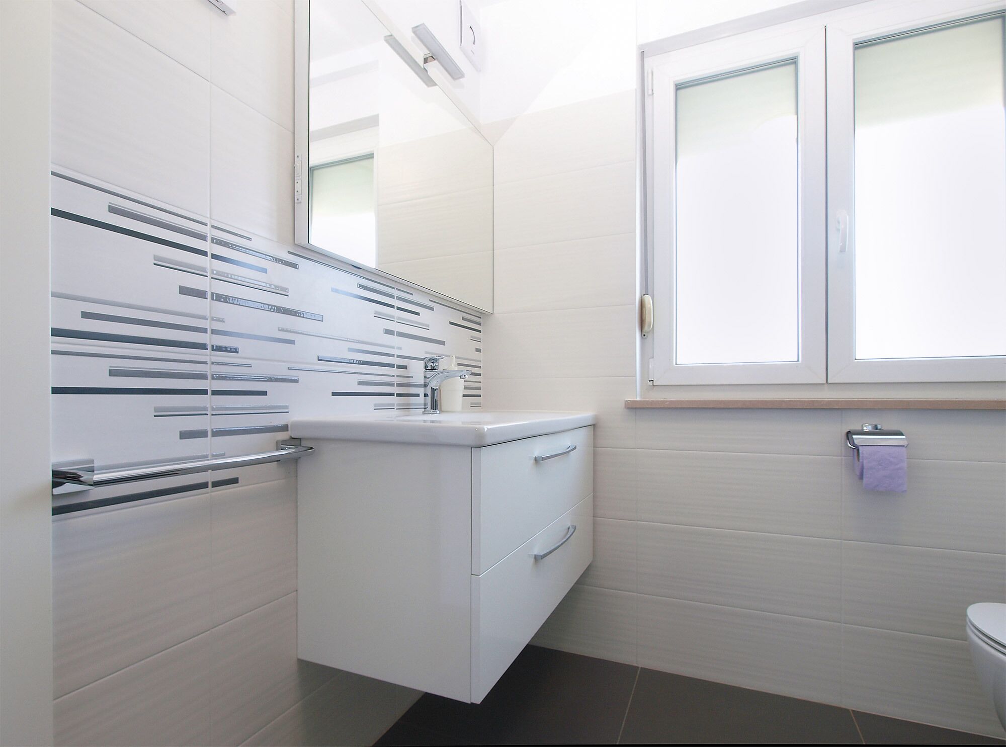 A modern bathroom with a white vanity, a window with frosted glass, and a towel rack.