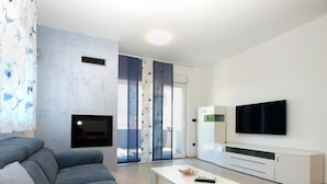 A modern living room with a grey sofa, a white coffee table, a flat-screen TV, and a fireplace. - House 1939 (Pula)