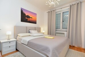Un dormitorio con cama, mesitas de noche, lámpara, cuadro y ventana con cortinas.