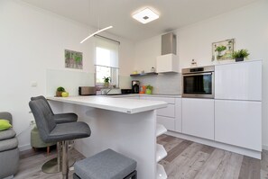 Una cocina moderna con armarios blancos, horno empotrado y una barra con una silla gris.