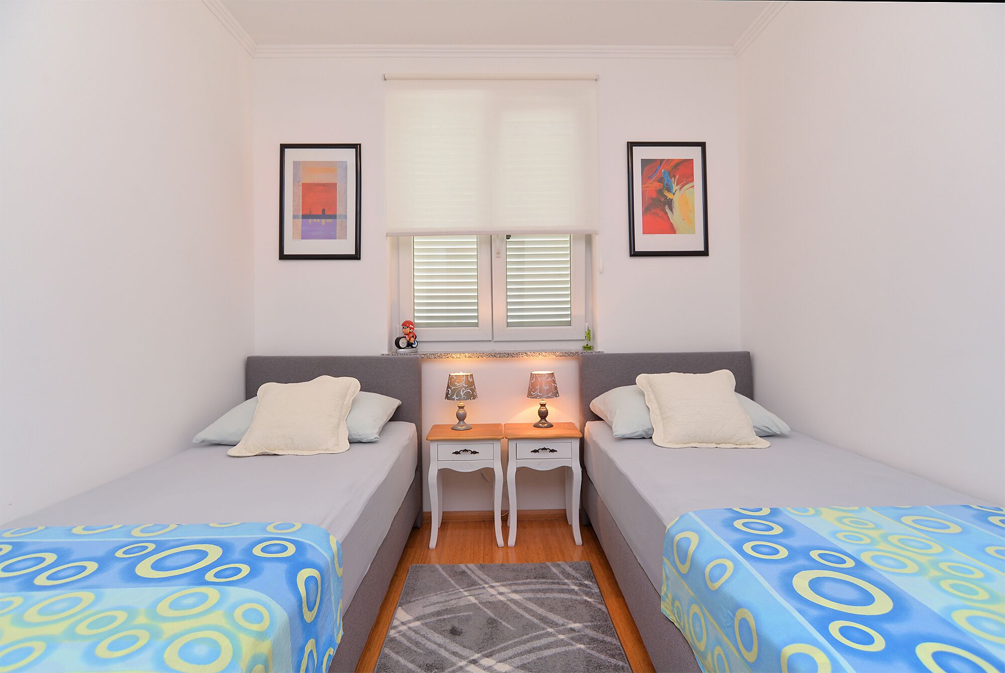 A small, well-lit bedroom with two single beds, a desk, and two bedside tables.