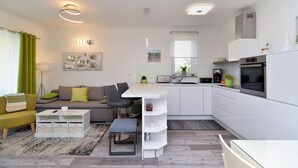 Un apartamento moderno con sala de estar, cocina y comedor. Cuenta con un sofá, una mesa de centro, una mesa de comedor y una cocina equipada con estufa y lavaplatos.