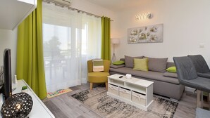 Una sala de estar moderna con un sofá gris, una mesa de centro blanca y un sillón amarillo. Hay un ventanal con cortinas verdes, una lámpara de pie y un aplique de pared.