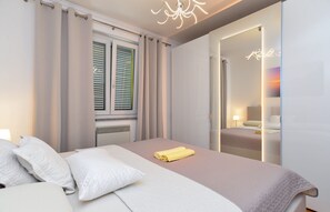 A modern bedroom with a bed, curtains, a radiator, and a mirror. - Apartment 1941 (Pula)