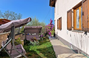 A narrow pathway leading to a house with a garden. There is a covered outdoor seating area with a table and chairs.