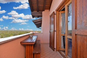A balcony with a wooden bench, a potted plant, and a view of a distant landscape.