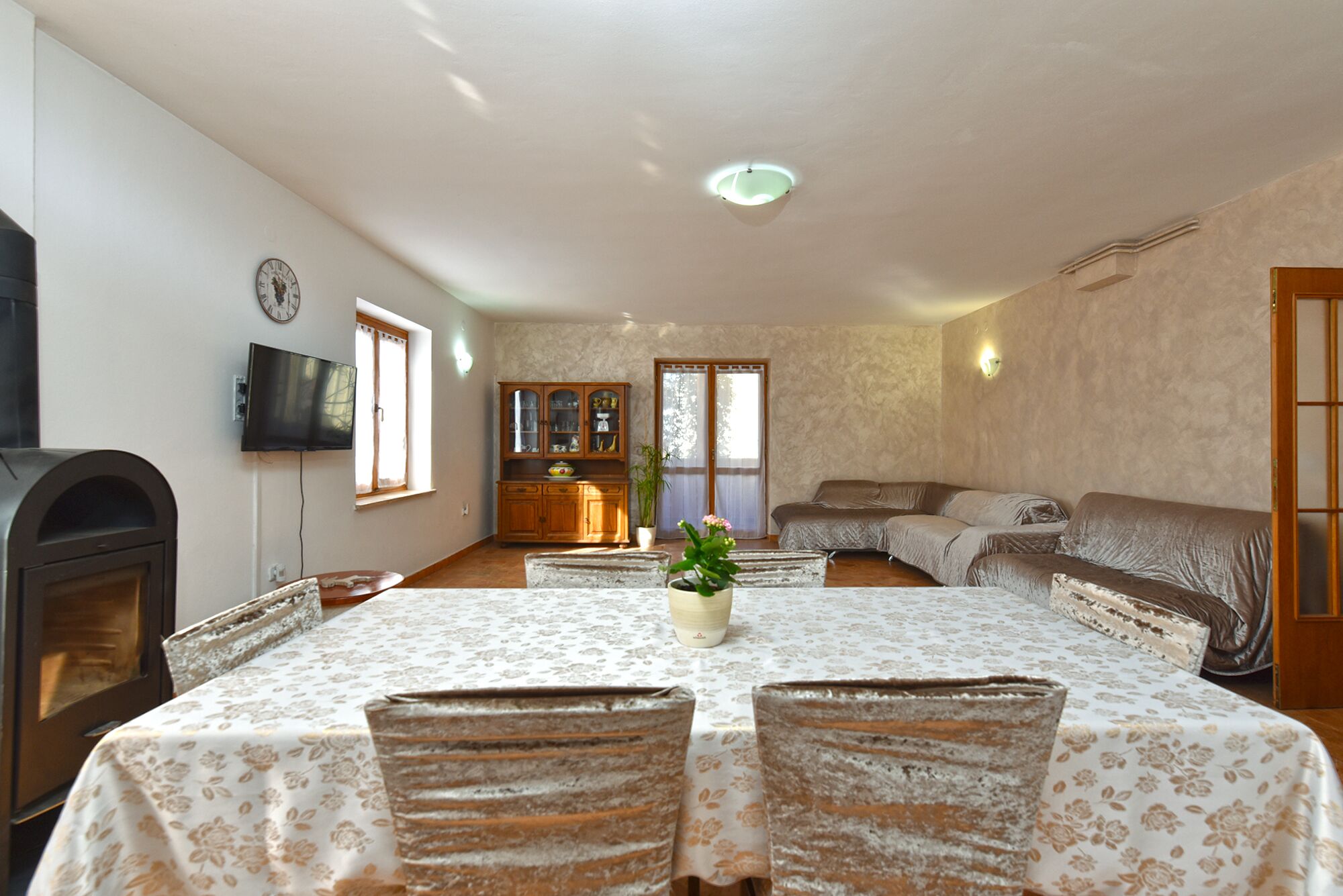 A spacious living room with a fireplace, a dining area with a table and chairs, a sofa, and a television mounted on the wall.