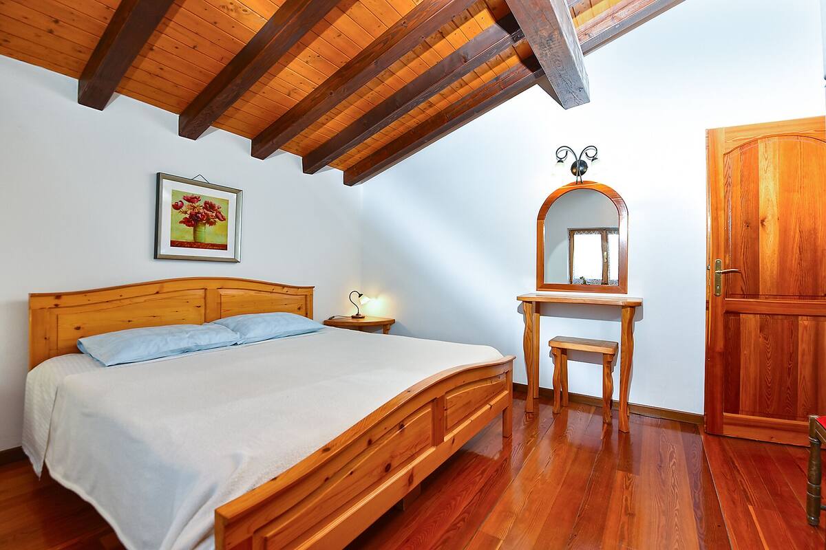 A bedroom with a wooden bed, a nightstand, a desk with a mirror, and a wardrobe.