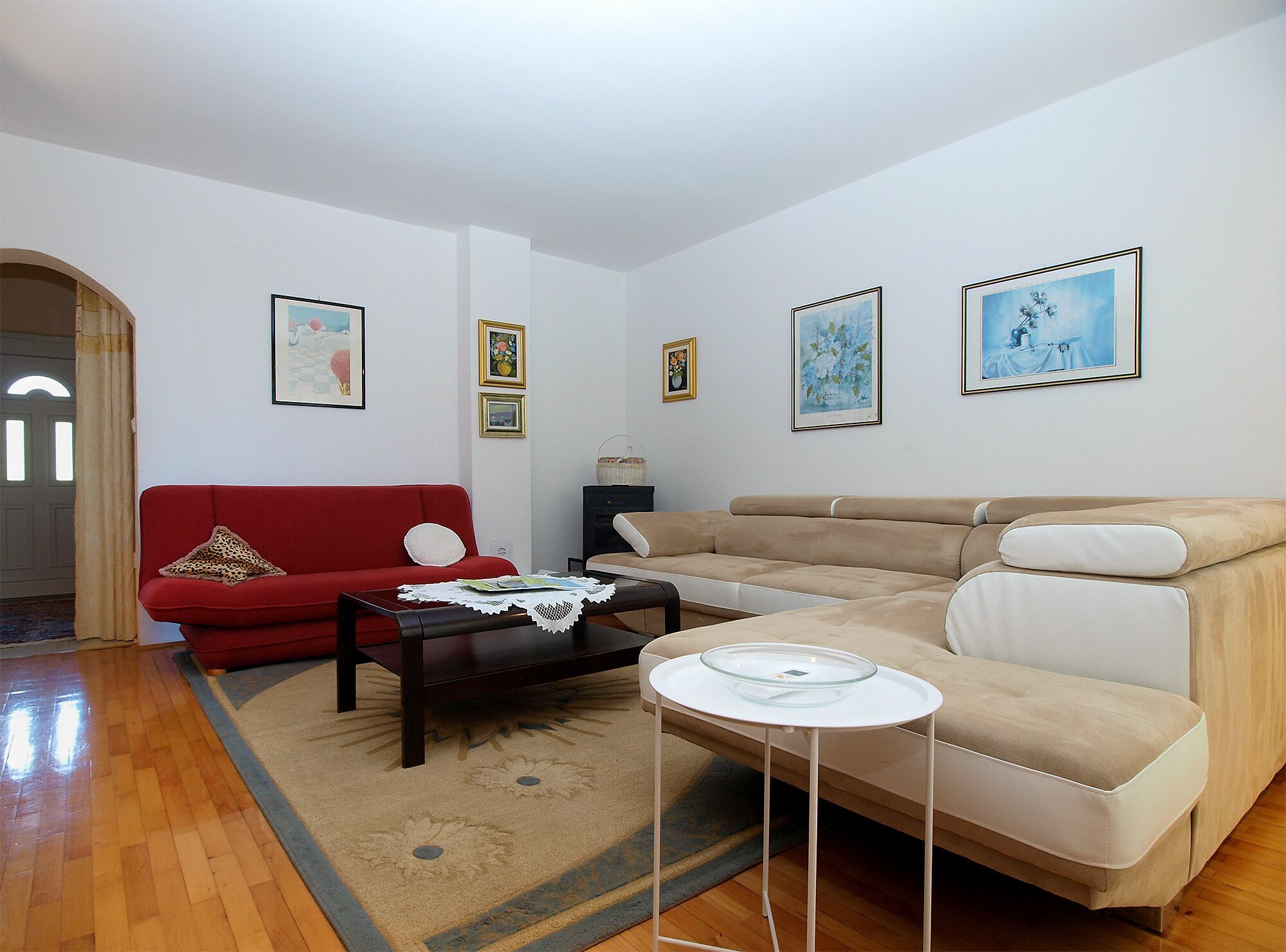 Un salon avec un canapé rouge, un canapé beige, une table basse en verre et un tapis.