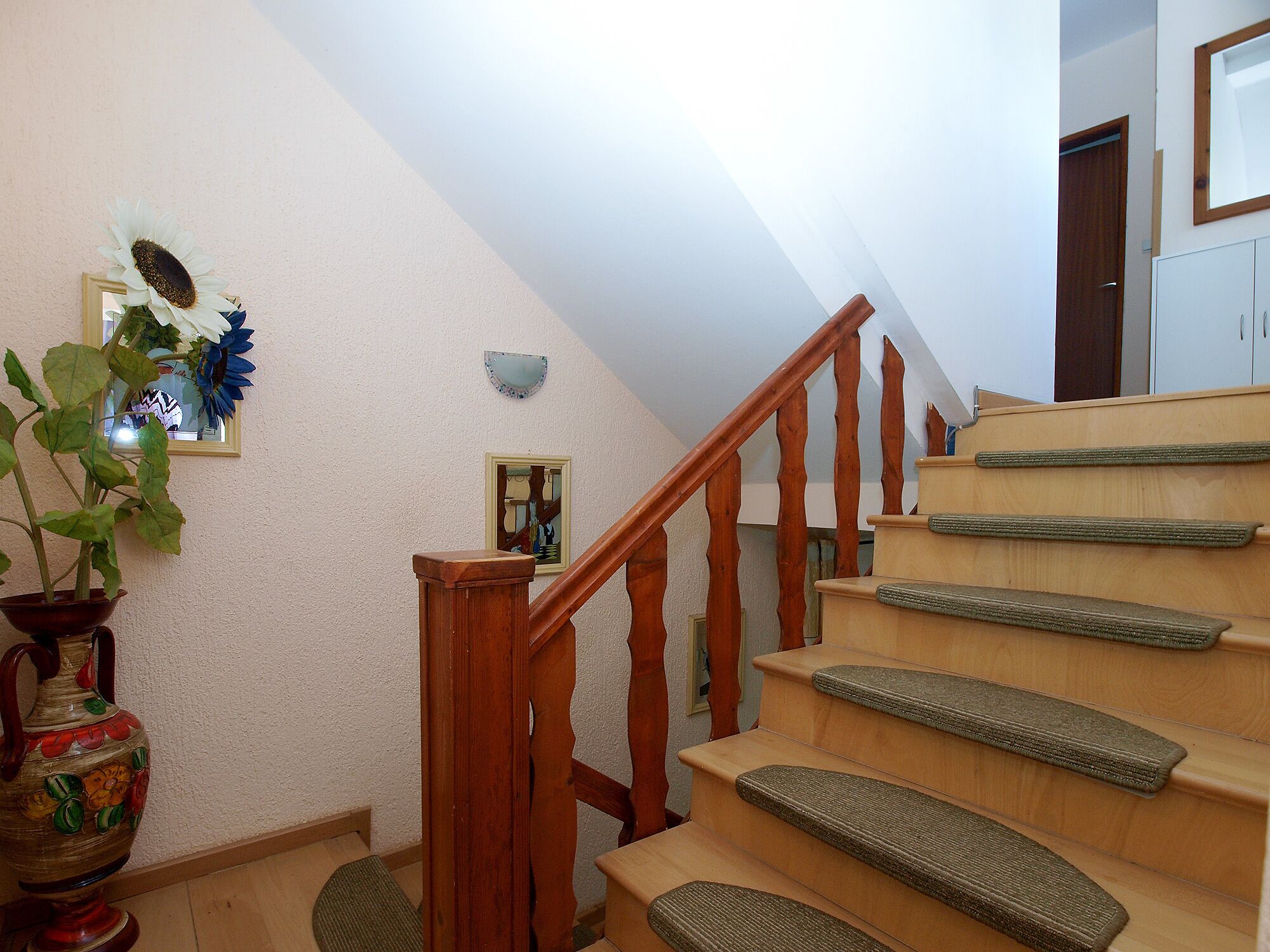 Eine Treppe mit Holzstufen und einem Holnänder, die zu einer Zwischenebene mit einem an der Wand befestigten Spiegel und einem gerahmten Bild führt.